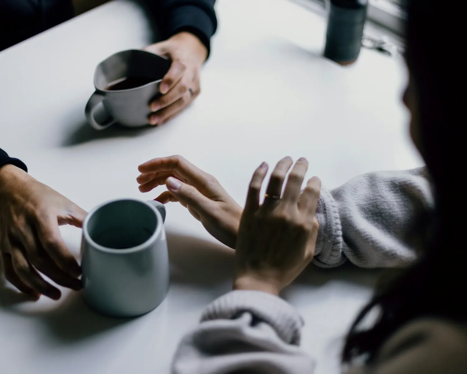 Handen van twee mensen in gesprek aan tafel, met een kop thee
